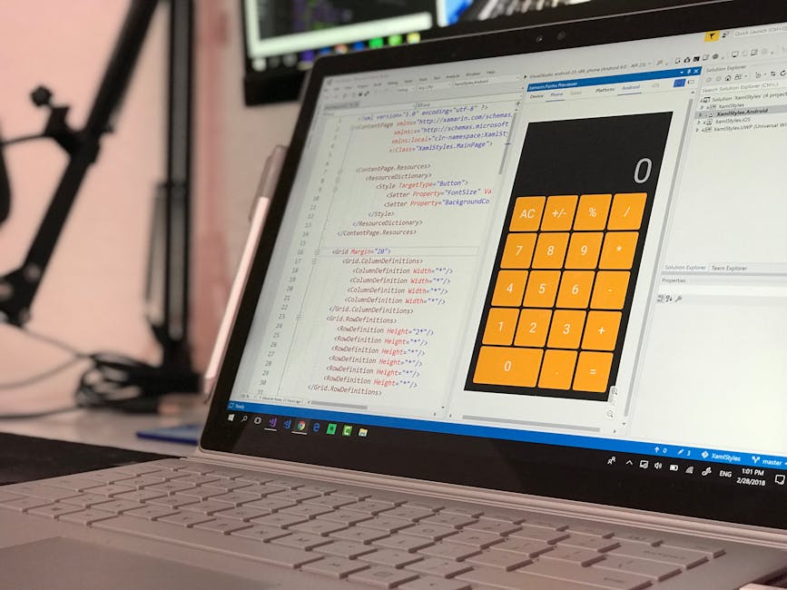 A person working on a laptop computer placed on a dark surface, with the screen displaying a code editor with lines of programming code in different colors such as green, blue, and white on a dark bac