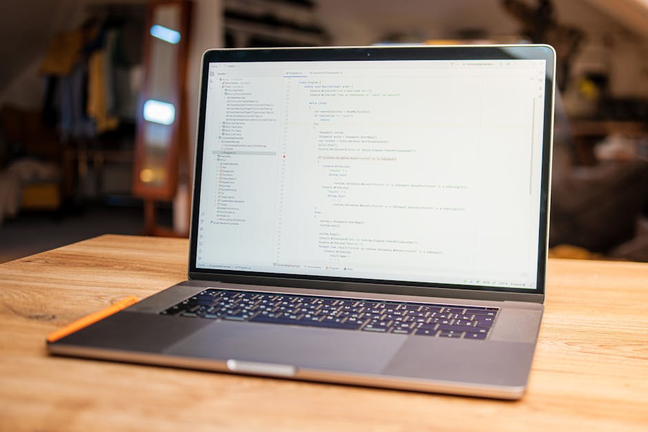 A close-up view of a laptop on a wooden surface displaying lines of computer code with a dark background, alongside a ceramic coffee mug with a printed message that reads 'This coffee is making me awe