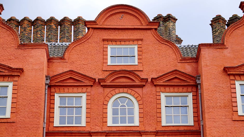 A row of Victorian-style terraced houses in NW6, featuring ornate white metalwork balconies and large bay windows, situated on a hillside with a brick retaining wall and small landscaped front gardens